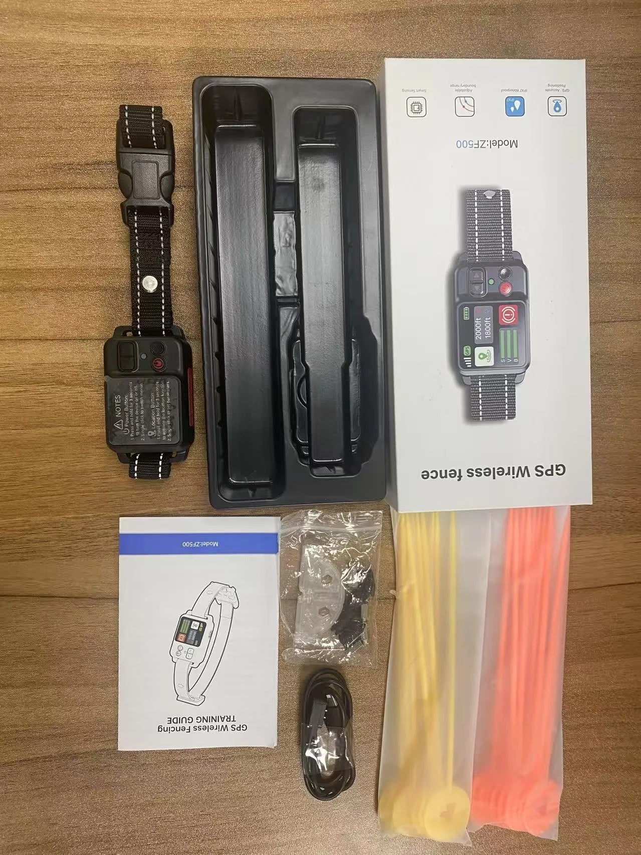 GPS wireless fence system components including collar, packaging, and accessories on a wooden surface.